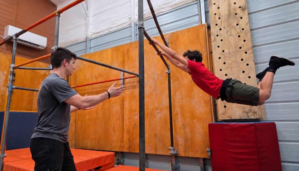 Blue Ridge Motion coach spotting a teen swinging on a parkour bar