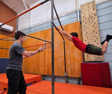 Blue Ridge Motion coach spotting a teen swinging on a parkour bar