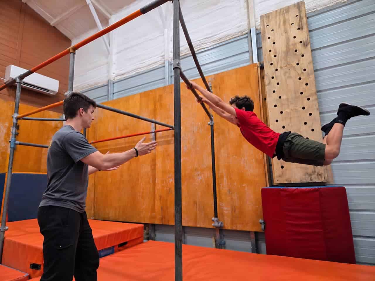 Blue Ridge Motion coach spotting a teen swinging on a parkour bar